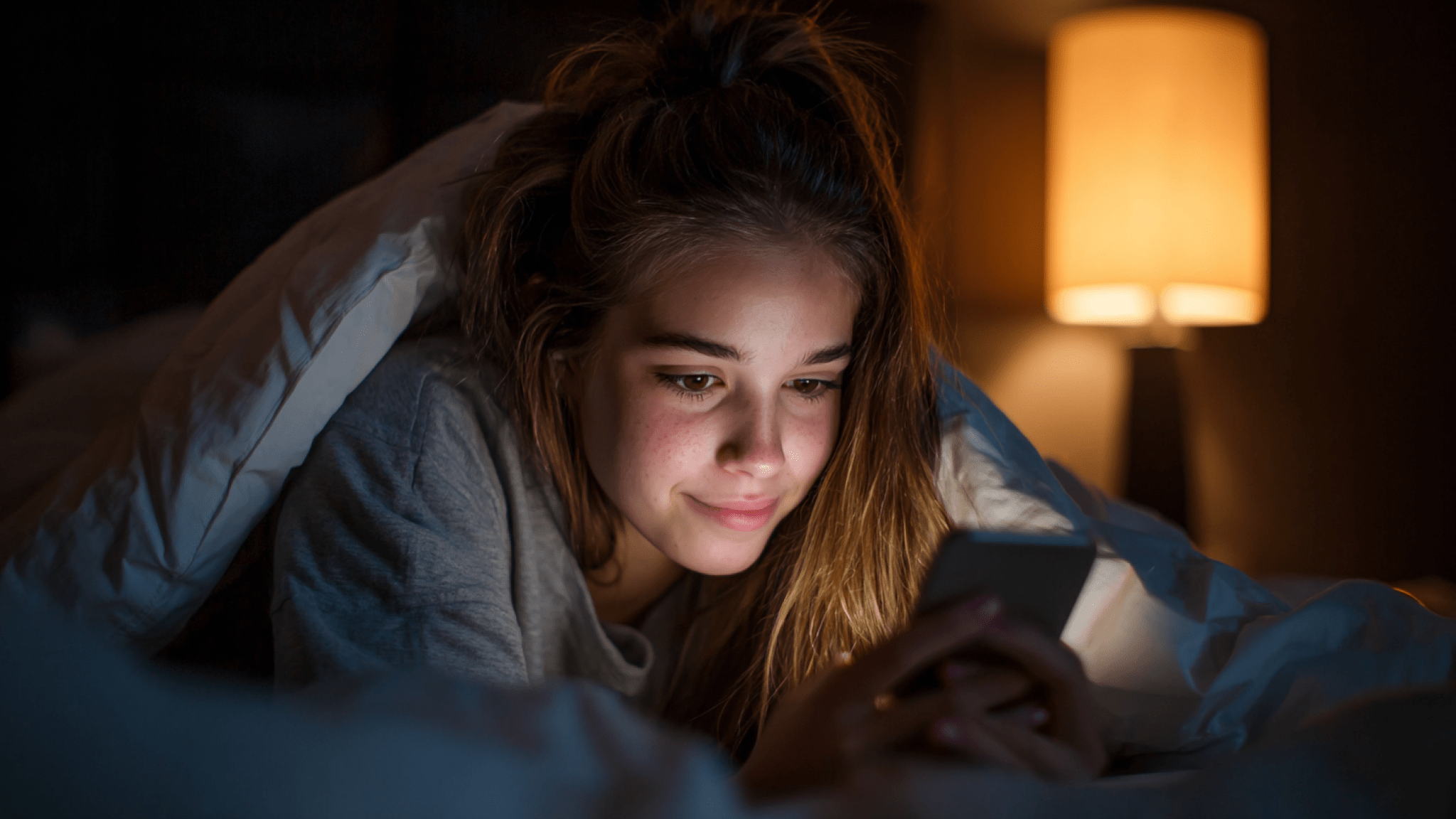 Flicka som ligger i säng och läser på mobil