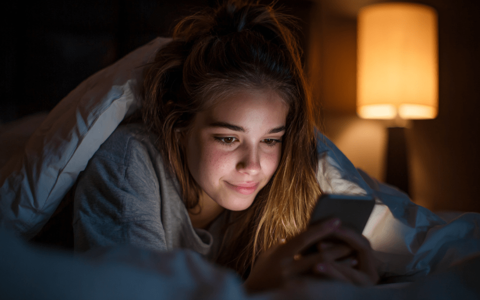 Flicka som ligger i säng och läser på mobil